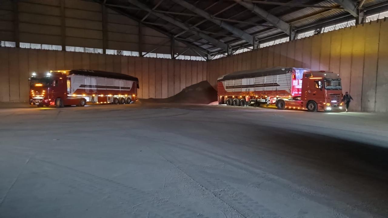 Trucks inside grain warehouse with bulk commodity stockpile